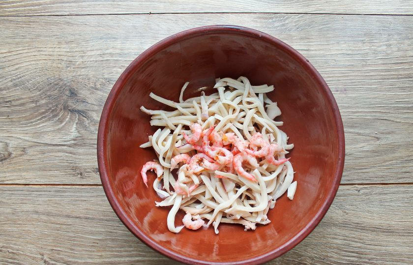 1. Этап. Салат с кальмарами, креветками и кукурузой: Креветки отварите в течение 3 минут после закипания в соленой воде. Креветки почистите и выложите в миску с кальмарами.