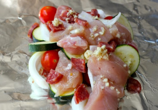 1. Этап. Курица с овощами в фольге: 6. Очистить луковицу и нарезать. В данном случае блюдо будет порционным. На небольшой кусочек фольги выложить часть овощей и курицы. Добавить несколько кусочков колбасы (при желании) для аромата.