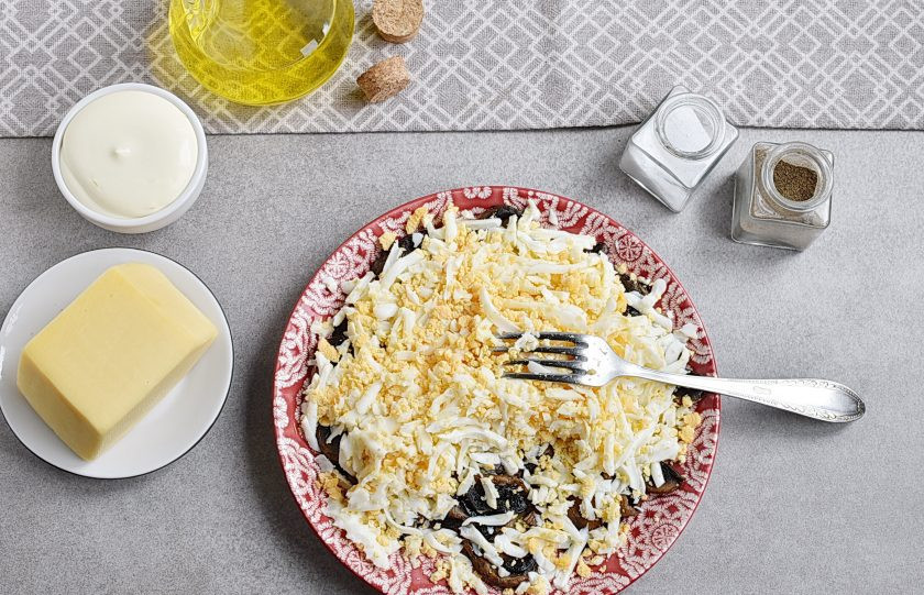 1. Этап. Простой салат с шампиньонами жареными: Готовые грибы выложите на салатную тарелку, посолите и поперчите по вкусу. Перец гораздо лучше брать свежемолотый. Еще теплые грибы посыпьте слоем тертых крутых яиц. И снова немного посолите и поперчите.