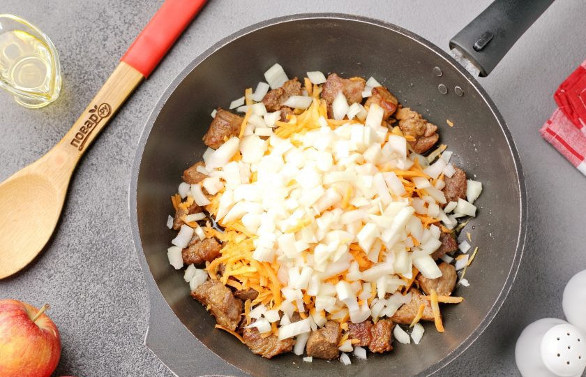 1. Этап. Мясо тушеное с капустой и яблоками: Добавьте тертую морковь и нарезанный кубиками лук.