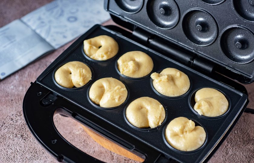 1. Этап. Пончики в мультипекаре: Установите на мультипекаре панели для приготовления пончиков, разогрейте мультипекарь, смажьте тонким слоем растительного масла все рабочие поверхности (достаточно будет одного раза), отсадите тесто из кондитерского мешка, заполняя половинки формочек.