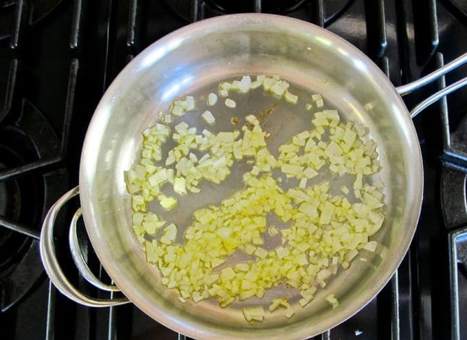 1. Этап. Шакшука с сыром: 1. Сначала в глубокой сковороде разогрейте масло. Добавьте в него мелко нашинкованный лук. Обжарьте кусочки в течение 11 минут, постоянно помешивая. Затем добавьте нарубленный чеснок. Готовьте овощи вместе 2 минуты.