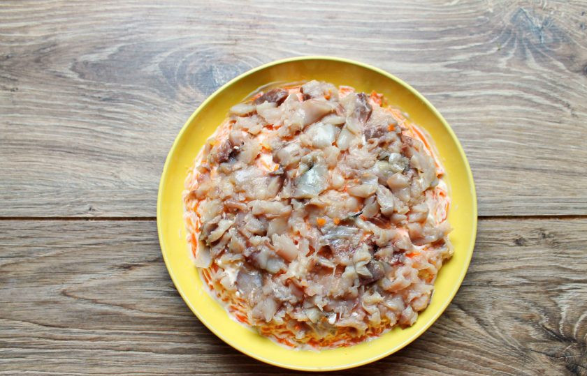 1. Этап. Селёдка под шубой с двумя видами рыбы: Скумбрию порежьте на кусочки, тщательно убирая кости и выложите на морковный слой, равномерно распределив.