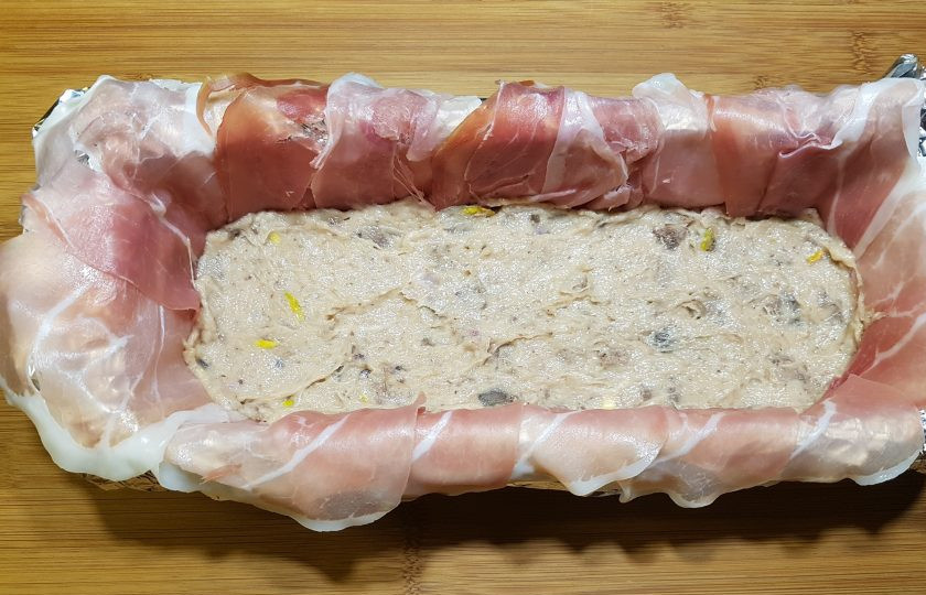 1. Этап. Террин из курицы с фисташками: Удлиненную форму для выпечки застелите фольгой. Смажьте маслом и выложите кусочки бекона по всему периметру формы внахлест. Выложите на дно половину приготовленного фарша, утрамбуйте.