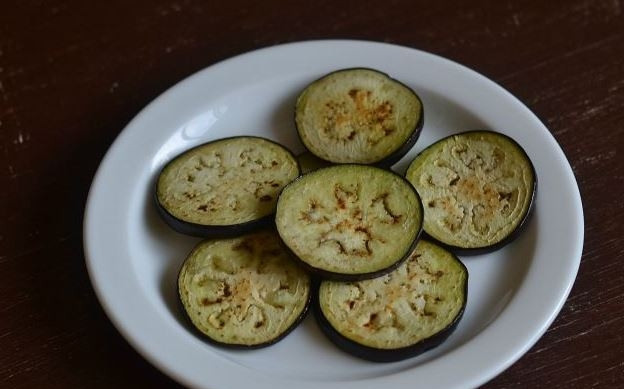 1. Этап. Баклажаны, запеченные с чесноком: Разогрейте на плите сковородку с антипригарным покрытием. Обжарьте кружочки баклажанов с обеих сторон по пять минут до золотистого цвета на маленьком огне.