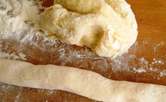 1. Этап. Ленивые картофельные вареники с грибами: Разделите картофельное тесто на две равные части. Скатайте из него два жгута, присыпая рабочую поверхность или разделочную доску мукой, чтобы тесто не прилипало.