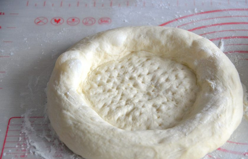 1. Этап. Лепешки Оби-нон: Через 30 минут можно окончательно формовать лепешки. Растяните лепешку в стороны, примяв центр лепешки, но оставив нетронутыми края. Поскольку нет специального инструмента, можно воспользоваться молоточком для отбивания мяса. Сделайте в центре лепешки 