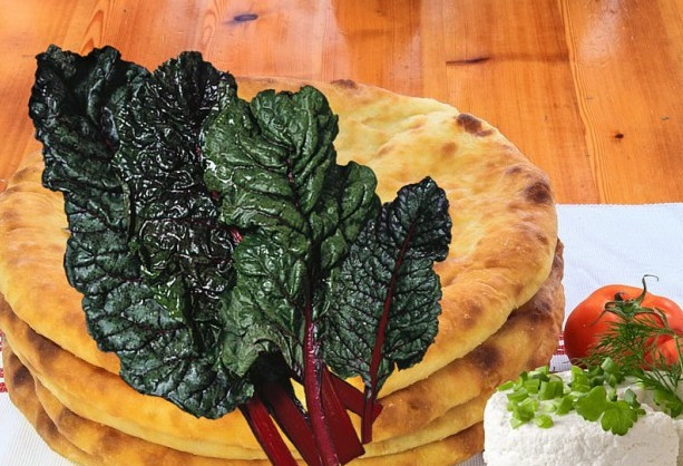 1. Этап. Осетинский пирог со свекольной ботвой: 6. Шар сплющите в лепешку. В центре сделайте отверстие для пара. Выпекайте 20 минут. Температуру в духовом шкафу предварительно доведите до 220 градусов. Достаньте пирог и полейте топленым маслом. Накройте тканью на 10 минут. Затем нарезайте и пробуйте.