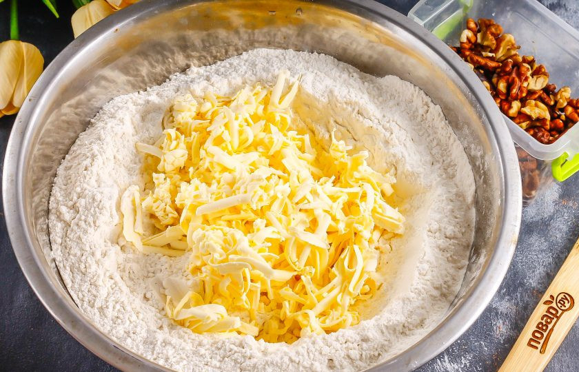 1. Этап. Торт Наполеон с грецкими орехами: Высыпьте муку в глубокую емкость, добавьте туда же щепотку соли и сахарный песок. Натрите сливочное масло на терке с крупными ячейками, подморозив его сначала в морозилке примерно 10 минут.