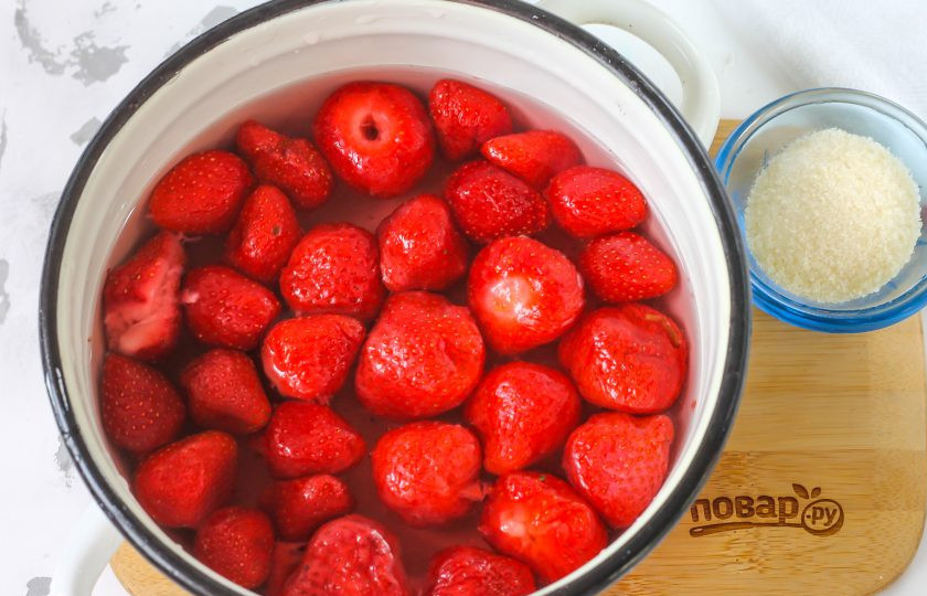 1. Этап. Клубничное конфи для торта: Клубнику промойте в воде, удалите черенки и выложите в глубокую емкость. Влейте 1 стакан теплой воды и поместите емкость на плиту, добавив сахарный песок.