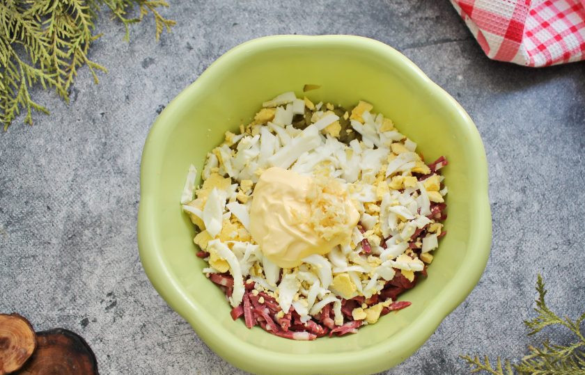 1. Этап. Салат Гнездо глухаря с колбасой: Яйцо очистите, порежьте и добавьте в салатник. Выложите майонез и измельченный чеснок, посолите.