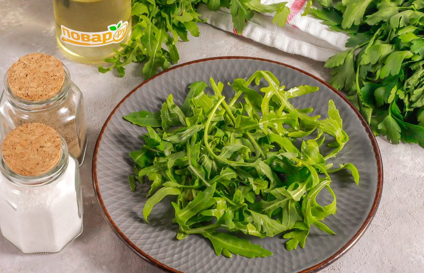 1. Этап. Салат с адыгейским сыром и помидорами: Промойте рукколу в воде, срежьте стебли и выложите зелень на тарелку.