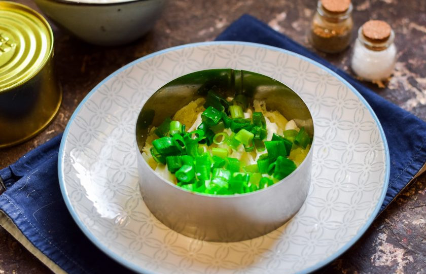 1. Этап. Мимоза с консервой: Зеленый лук сполосните и мелко нарежьте, посыпьте салат.