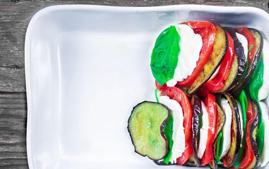 1. Этап. Салат с запеченными баклажанами: 2. Вымойте листики базилика. Нарежьте моцареллу кружочками. Возьмите форму для запекания и уложите ингредиенты поочерёдно: сыр, базилик, баклажан, томат.