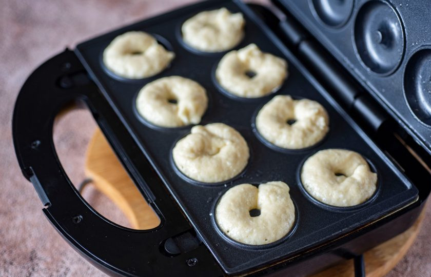 1. Этап. Творожные пончики в мультипекаре: На мультипекарь установите рабочие поверхности с формочками для пончиков. Каждую формочку смажьте тонким слоем растительного масла и включите разогреваться. В хорошо разогретые формочки выложите чайной ложкой тесто, заполняя половинки формочек, как на фото.