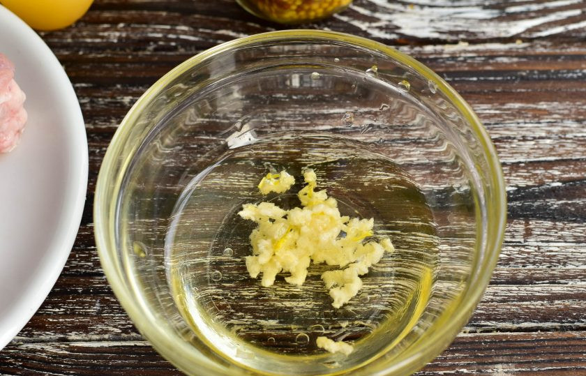 1. Этап. Запеченное мясо на Новый год: Влейте в миску масло и выдавите чеснок.