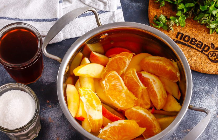 1. Этап. Алкогольный компот: Очистите мандарин от кожуры, удалите белый слой с поверхности фрукта. Разделите плод на дольки и добавьте в емкость к яблочной нарезке.