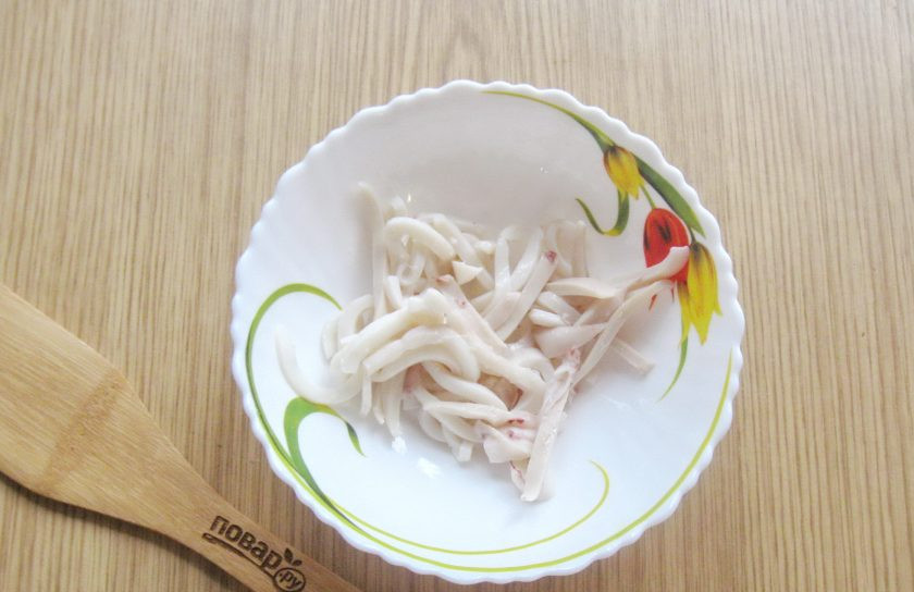 1. Этап. Салат с кальмарами и маринованным луком: Немного охладите кальмар и нарежьте соломкой. Выложите в салатник.