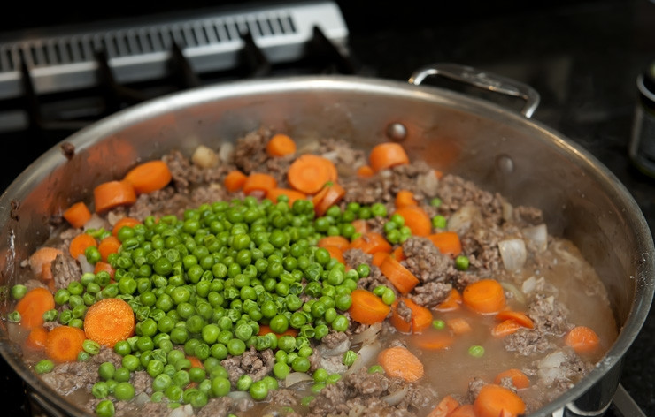 1. Этап. Пастуший пирог: Добавляем говяжий бульон и хорошенько все перемешиваем. Добавляем горох и морковь и снова перемешиваем, уменьшаем огонь и даем пару минут покипеть. Соус должен сгуститься, а овощи стать мягче. Если соус слишком загустел, то можно еще немного добавить бульона.