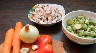 1. Этап. Запеканка из брюссельской капусты: Брюссельскую капусту хорошенько промойте под проточной водой, разрежьте каждую на две части. Шампиньоны почистите ножом, промойте и нарежьте небольшими пластинками. Морковку поскоблите ножом и натрите на терке, лук с болгарским перцем вымойте, очистите и нашинкуйте на тонкие полосочки.