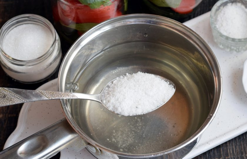 1. Этап. Помидоры с вишневыми листьями на зиму: Воду из банок слейте в сотейник, установите на огонь, вскипятите, добавьте сахар и соль, полностью их растворите, снимите с огня.