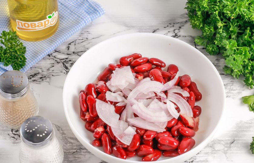 1. Этап. Салат из говядины и консервированной красной фасоли: Фасоль выложите в глубокую емкость: миску или салатник. Промойте и чистите луковицу, разрежьте пополам и нарежьте половину полукольцами. Добавьте в емкость.