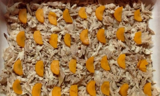 1. Этап. Диетический холодец: Сваренное мясо курицы разбираем на кусочки и выкладываем в широкую емкость для холодца. Сверху раскладываем кусочки моркови. Чеснок пропускаем через пресс и выкладываем сверху.