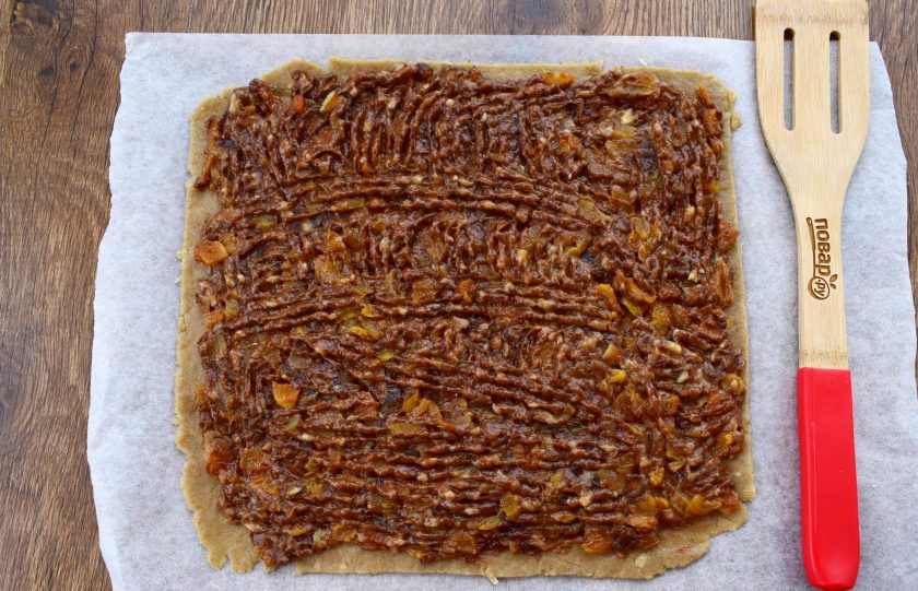 1. Этап. Ржаное пирожное постное: Духовку включите и разогрейте до 180 °C. Тесто разделите на 2 равные части. Одну раскатайте в тонкий квадратный пласт. Распределите по нему всю начинку равномерным слоем.