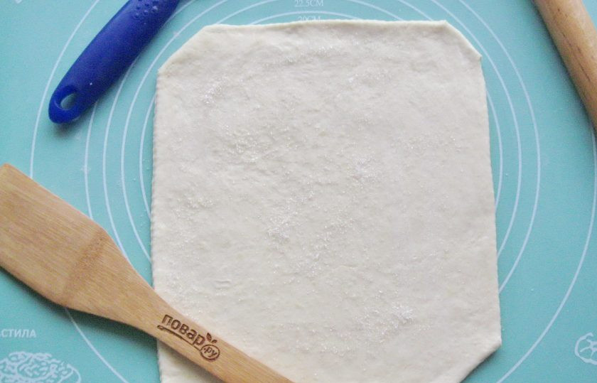 1. Этап. Слоеные язычки на пиве: После достаньте тесто из холодильника и раскатайте его пласт толщиной 3-4 мм. Смажьте тесто водой и посыпьте сахаром.