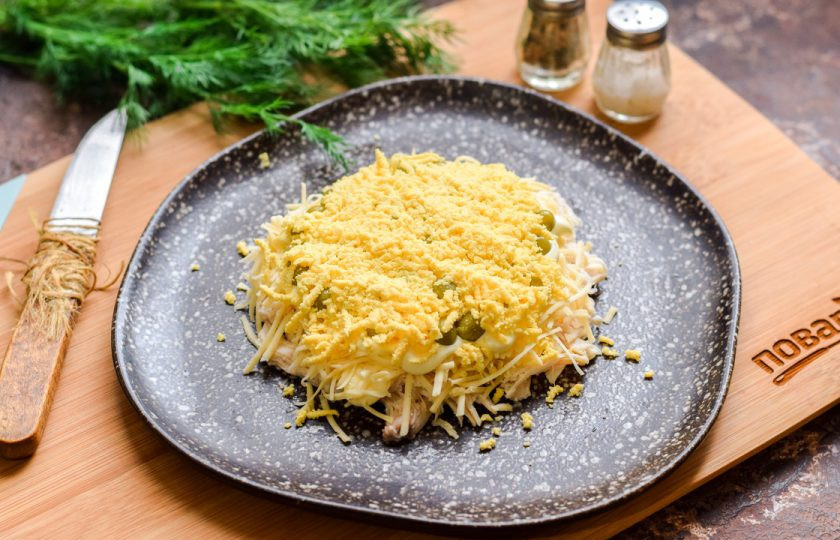 1. Этап. Слоеный салат с курицей Бычок: Куриные яйца разделите на желтки и белки. Натрите желтки на мелкой терке и выложите поверх горошка. Столовую ложку желтков отложите в сторонку, для декора.