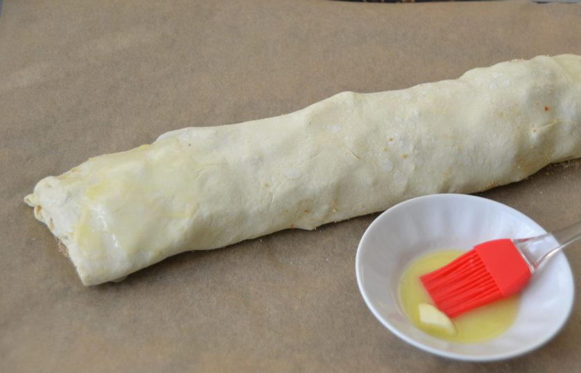 1. Этап. Ленивый яблочный штрудель: Перенесите штрудель на лист для выпечки, смажьте сверху сливочным маслом.