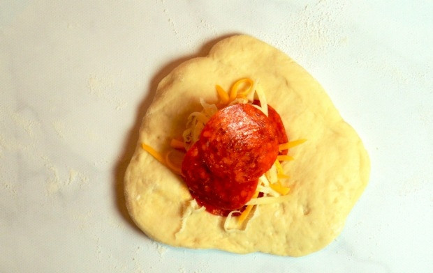 1. Этап. Булочки для перекуса: 9. Каждый кусочек теста раскатайте в небольшую лепешку, по центру выложите несколько ломтиков колбасы, затем добавьте 2 вида сыра.