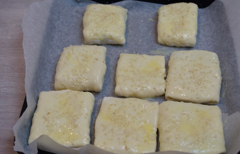 1. Этап. Хачапури из бездрожжевого слоеного теста: Сверните тесто с начинкой конвертиком. Закрепите плотно края, иначе при запекании через оставшиеся отверстия вытечет сыр. Поэтому все хорошо защипните. Уложите на противень. Смажьте взбитым яйцом, посыпьте кунжутом. Кунжут использовать не обязательно.