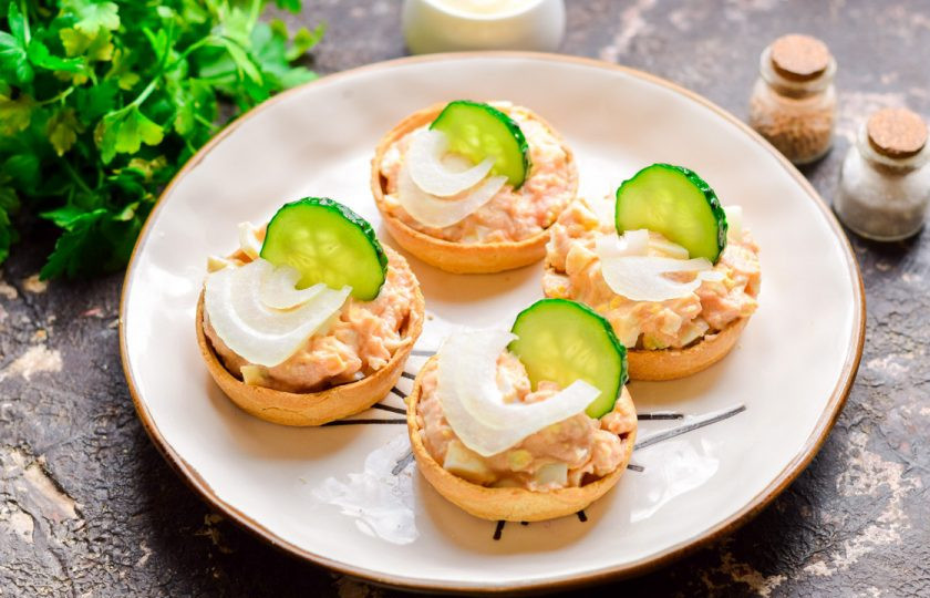 1. Этап. Тарталетки с икрой минтая: Добавьте в тарталетки немного нарезанного лука и дольку огурца.