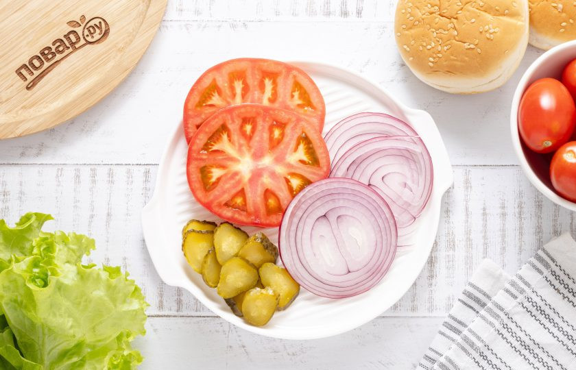 1. Этап. Соевые бургеры: Булочку для бургера разрежьте на 2 части, подсушите на сухой сковороде. Помидоры нарежьте кружочками, маринованные огурцы тонкими слайсами, а красный лук колечками.