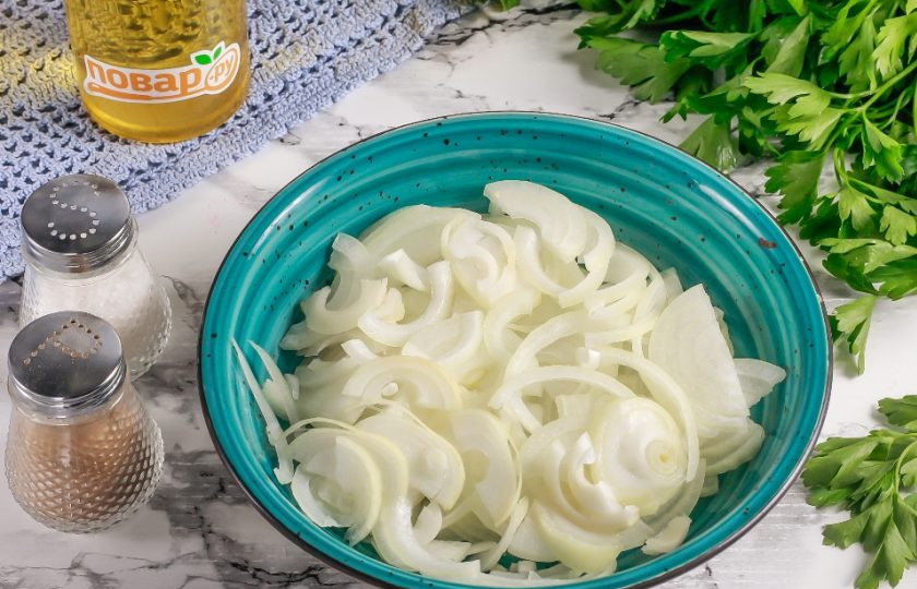 1. Этап. Маринованный лук с петрушкой: Очищенный и промытый лук разрежьте пополам и нарежьте тонкими полукольцами. Так поступите с каждой луковицей, выкладывая нарезку в глубокую емкость.