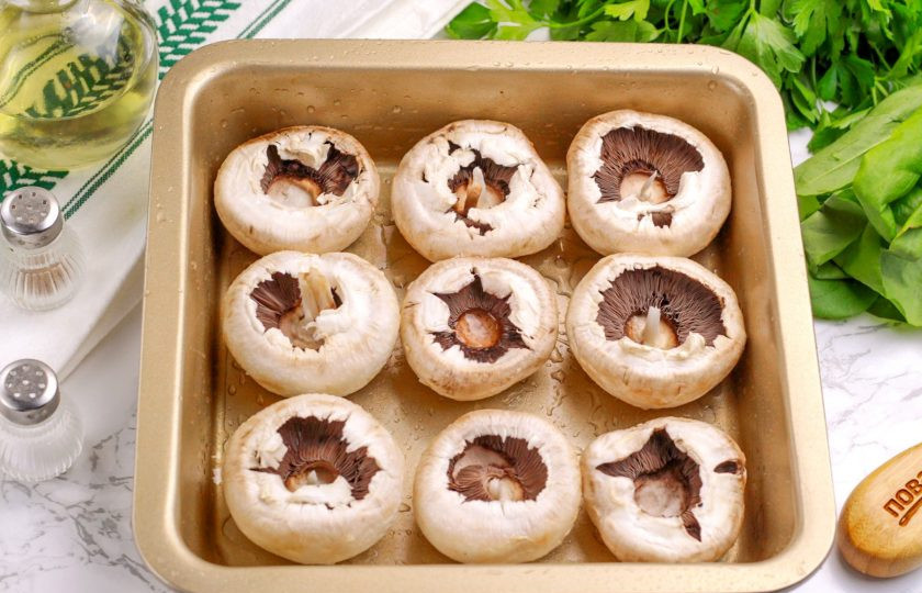 1. Этап. Шампиньоны с куриным фаршем: Шампиньоны промойте, аккуратно удалите ножки, а шляпки подсушите бумажными салфетками. Смажьте или сбрызните форму растительным маслом и выложите в нее шляпки грибов.