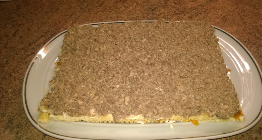 1. Этап. Слоеный торт с рыбой: 7. Берем второй корж. Снова промазываем слегка майонезом, и намазанной поверхностью аккуратно кладем на морковь. Снова смажем майонезом — и выкладываем рыбу, так же распределяем её вилочкой по всей поверхности коржа.