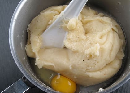 1. Этап. Сырные ньокки: Когда тесто полностью впитает влагу, снимите его с огня и добавляйте яйца по одному, вмешивая их в тесто с помощью лопатки.