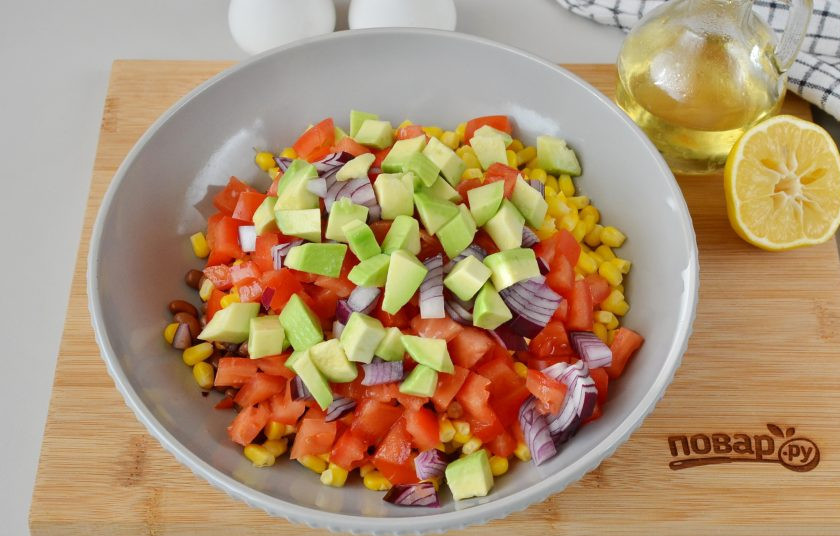 1. Этап. Овощной салат с фасолью и кукурузой: Авокадо вымойте, разрежьте по косточке на две половинки, снимите кожуру, нарежьте авокадо кубиками, сбрызните лимонным соком и выложите в салат.