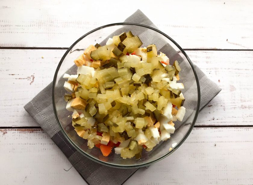 1. Этап. Оливье с печенью: Огурцы нарежьте маленькими кубиками и выложите в тарелку.