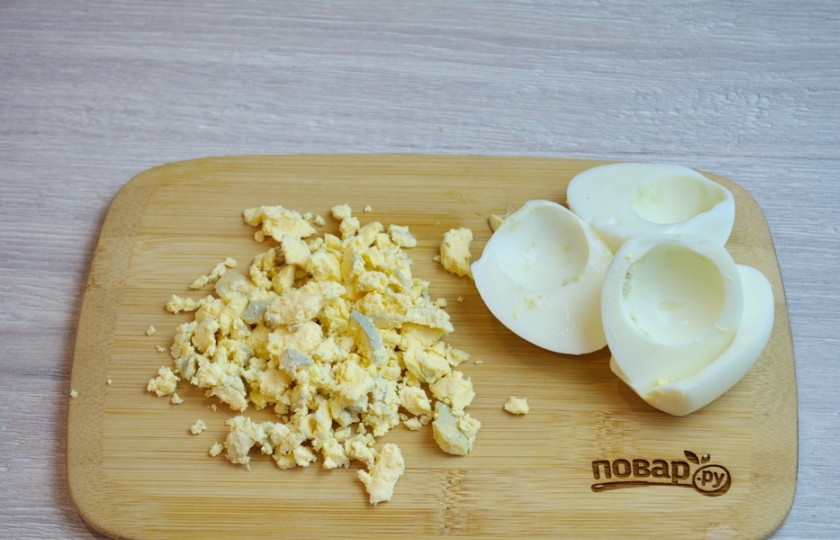 1. Этап. Новогодний салат Куранты: 5. Отварные куриные яйца очистите и разрежьте пополам. Извлеките желток. Нарежьте его и добавьте в салат. Белки отложите для декора.