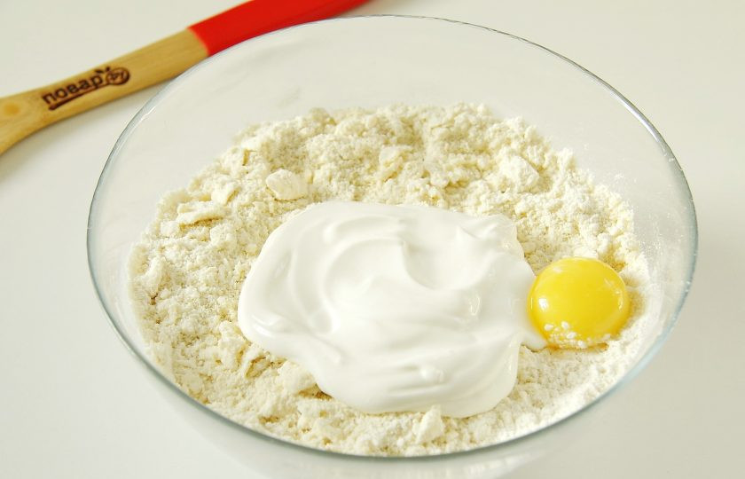 1. Этап. Слоеное печенье на сметане: Добавьте сметану и желток (белок нам понадобится чуть позже).