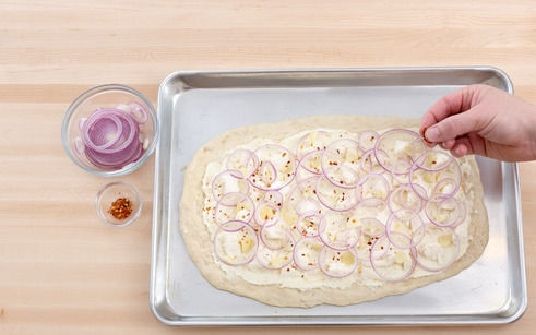 1. Этап. Пицца с творогом: 2. Раскатайте тонко тесто. Выложите творог и распределите ровным слоем. Присыпьте щепоткой соли и хлопьями перца. Выложите кольца лука и чеснок.