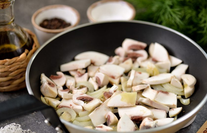 1. Этап. Бюджетный салат с куриными желудками и жареными грибами: Разогрейте в сковороде немного растительного масла, выложите в него очищенный и нарезанный репчатый лук, обжарьте его около минуты. Шампиньоны нарежьте тонкими пластинками, добавьте в сковороду, обжарьте вместе с луком около 5 минут.