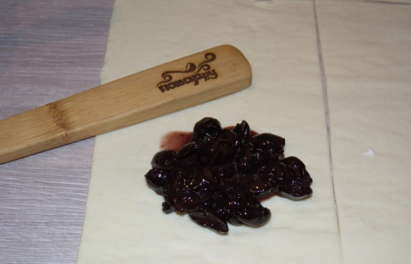 1. Этап. Конвертики из слоеного теста: Чтобы при запекании вишневая начинка не текла, добавьте к вишням столовую ложку крахмала. Перемешайте. По столовой ложке начинки на каждый корвертик выложите.