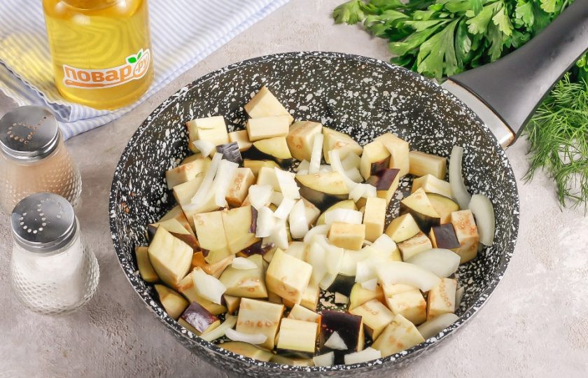 1. Этап. Шакшука с баклажанами и лимонной цедрой: Очистите лук от кожуры, срежьте хвостики с баклажана и промойте овощи в воде. Нарежьте баклажан средними кубиками, а лук — полукольцами. Разогрейте растительное масло в сковороде и выложите в нее овощные нарезки. Обжарьте все примерно 3-4 минуты.