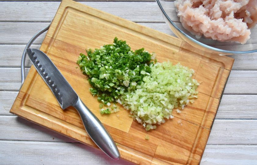 1. Этап. Момо с курицей: Мелко нарежьте стебель сельдерея и зеленый лук. Переложите зелень к куриному фаршу.