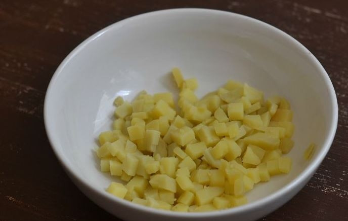 1. Этап. Салат с грудкой и грибами: В кастрюле вскипятите воду, картофель вымойте и положите в кастрюльку. Отварите его до готовности на плите, затем остудите и снимите кожицу. Нарежьте отварной картофель кубиками.