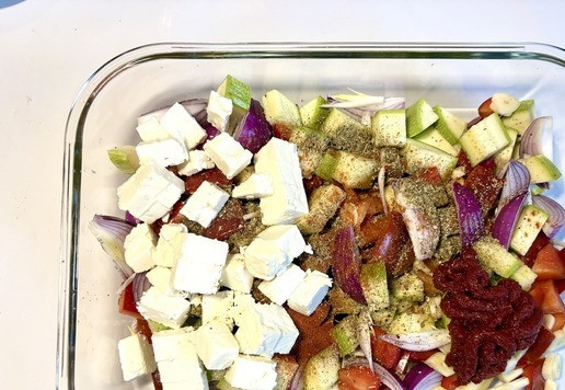 1. Этап. Паста с овощами и фетой из духовки: Положить овощи в форму для запекания, можно готовить сразу в сковородке, которую можно использовать в духовке. Посыпать овощи приправами ( розмарин, орегано, кайенский и чёрный перец, копчённую паприку, сахар), добавить томатную пасту, оливковое масло и фету.